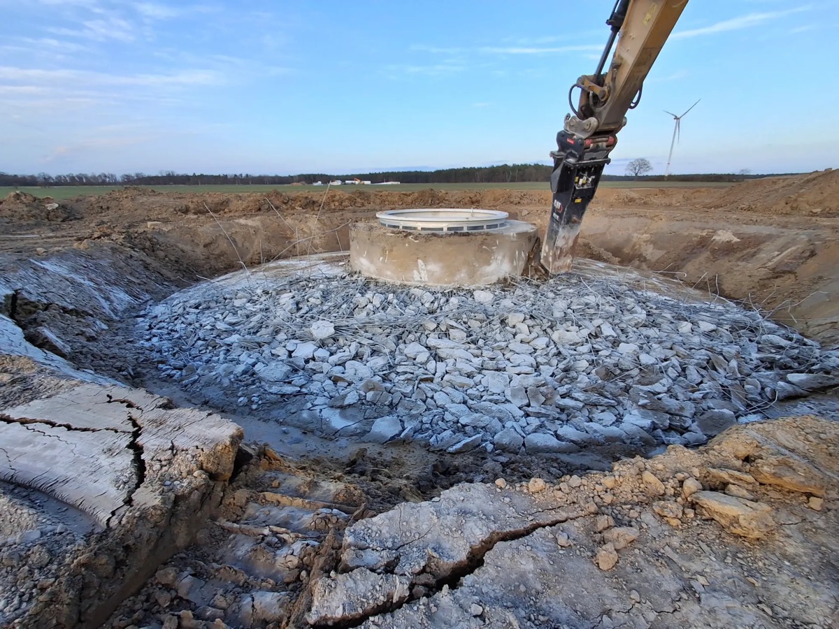 An excavator breaking up the concrete foundation of a wind turbine